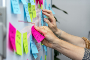 Two people are sticking post it notes on a whiteboard